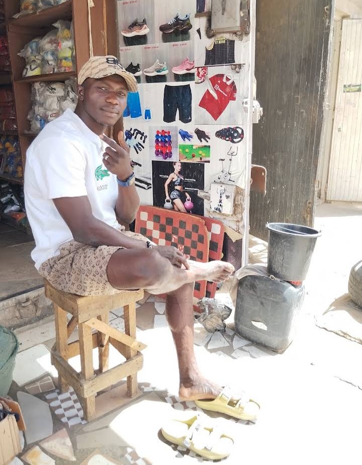 The owner of Ejyke Sports Store seated in front of the shop